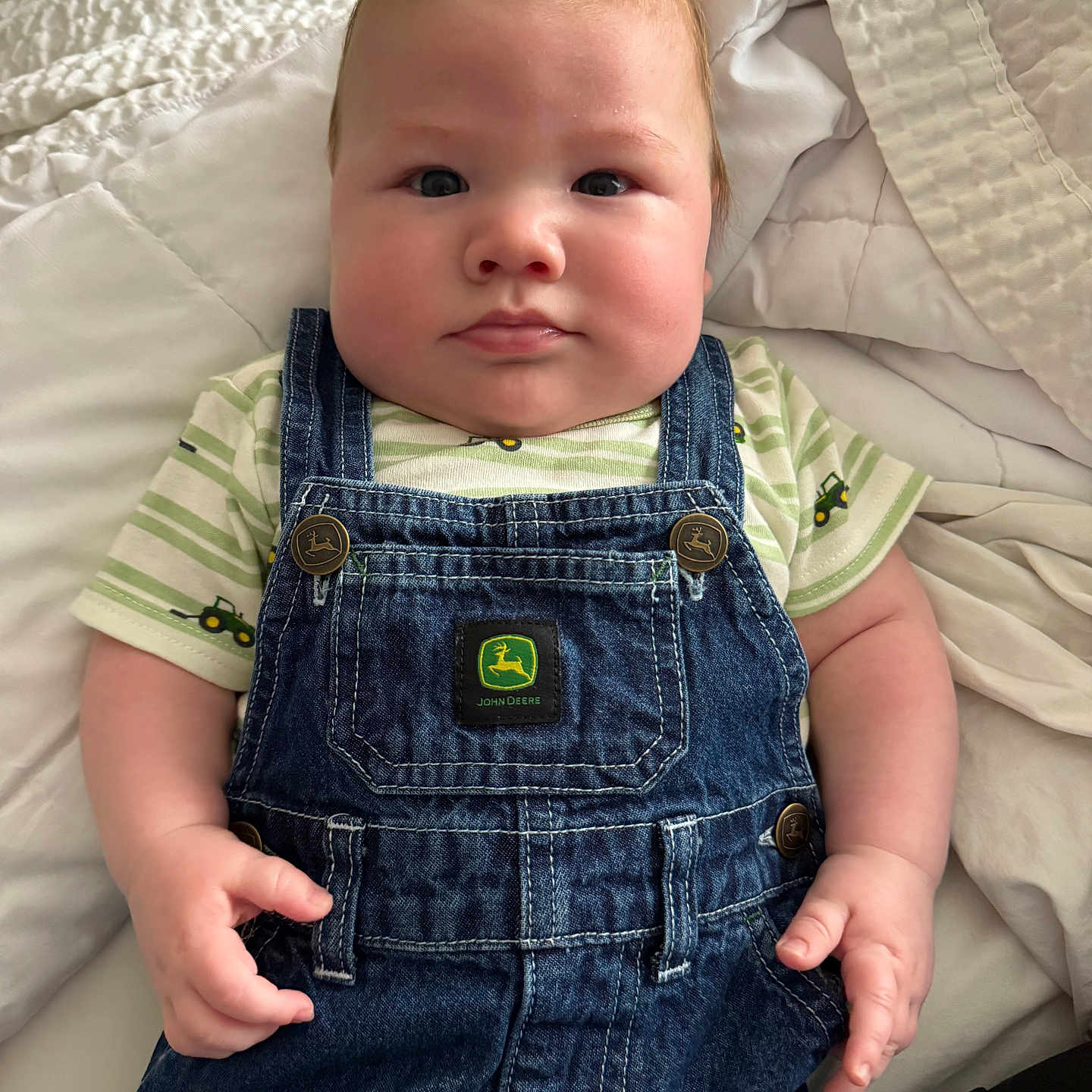 Jamie is registered to the contest to win money with this photo: baby, infant, child, denim_overalls, striped_shirt, cute, chubby_cheeks, bed, blanket, indoor, portrait, face, hands, clothing, casual, young, resting, light_skin, red_hair, closeup