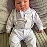 Jamie is registered to the contest to win money with this photo: baby, infant, white_clothing, bow_tie, suspenders, sitting, couch, gray_couch, footwear, shoes, portrait, indoors, cute, child, person, young, fashion, comfortable, texture, soft_fabric