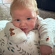 Jamie joined the competition — help win amazing prizes! baby, infant, face, blue_eyes, light_hair, teddy_bear_pattern, long_sleeves, cushion, floral_pattern, carpet, indoor, sofa, child, resting, curious, cozy, cute, portrait, person, home