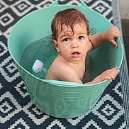 Côme participe au concours pour gagner de l'argent avec cette photo : toddler, child, bucket, water, wet_hair, indoor, carpet, patterned_rug, curious, gripping, bath_time, cute, small, person, expression, sitting, container, playful, young, face