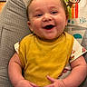 baby, infant, smiling, yellow_bib, baby_seat, cartoon_monkey, rainbow, happy, chubby_hands, cute, child, indoors, playful, colorful, clothing, portrait, closeup, joyful, expression, seated