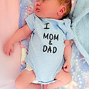 Phoenix is registered to the contest to win money with this photo: baby, newborn, sleeping, onesie, blue_clothing, blanket, infant, peaceful, cute, soft_texture, pastel_colors, child, human, skin, small_hands, small_feet, lying_down, indoors, portrait, love_message