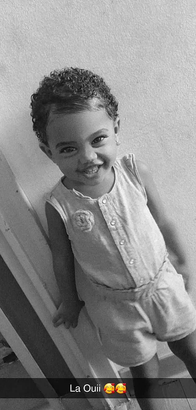 Naëhlya a rejoint le concours — aidez-le/la à gagner de superbes lots ! black_and_white, child, eyebrow, fashion_design, flash_photography, fun, hairstyle, happy, jheri_curl, joy, monochrome, monochrome_photography, person, room, s_curl, sleeve, smile, standing, style, toddler