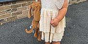 Darcie-Rae is registered to the contest to win money with this photo: toddler, child, dress, stuffed_animal, toy, outdoor, pavement, window, brick_wall, sandals, curly_hair, expression, sidewalk, building, basket, footwear, person, summer, casual, young_child