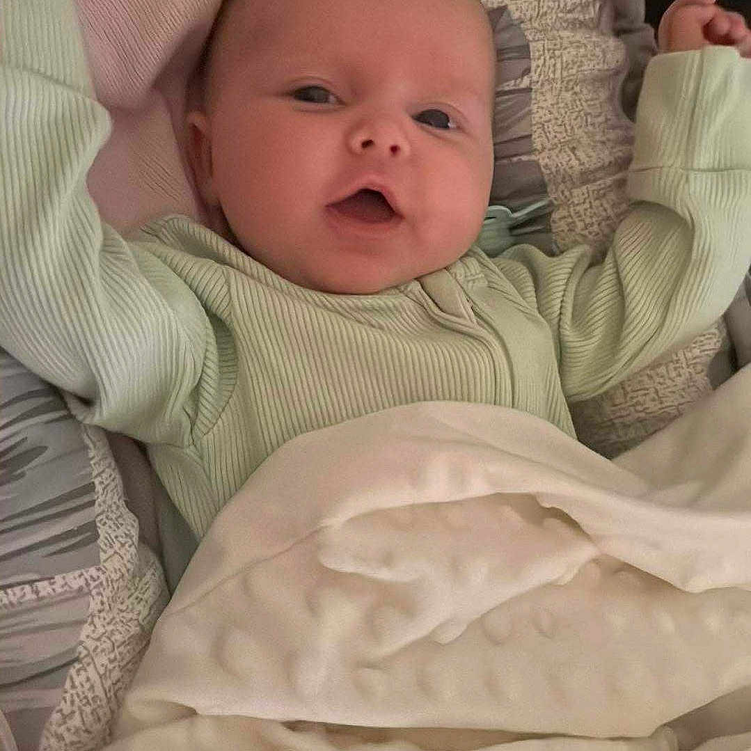 Amelia joined the competition — help win amazing prizes! baby, bed, blanket, clothing, comfort, cozy, cute, expression, face, furniture, happy, indoors, infant, infant_clothing, laying_down, person, portrait, sleeping_area, smiling, soft