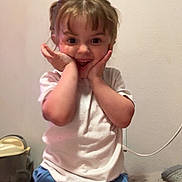 Willow is registered to the contest to win money with this photo: child, smiling, happy, indoor, white_shirt, blue_pants, butterfly_design, hands_on_face, expression, cute, young, person, wall, casual_clothing, furniture, home, playful, light, portrait, sitting
