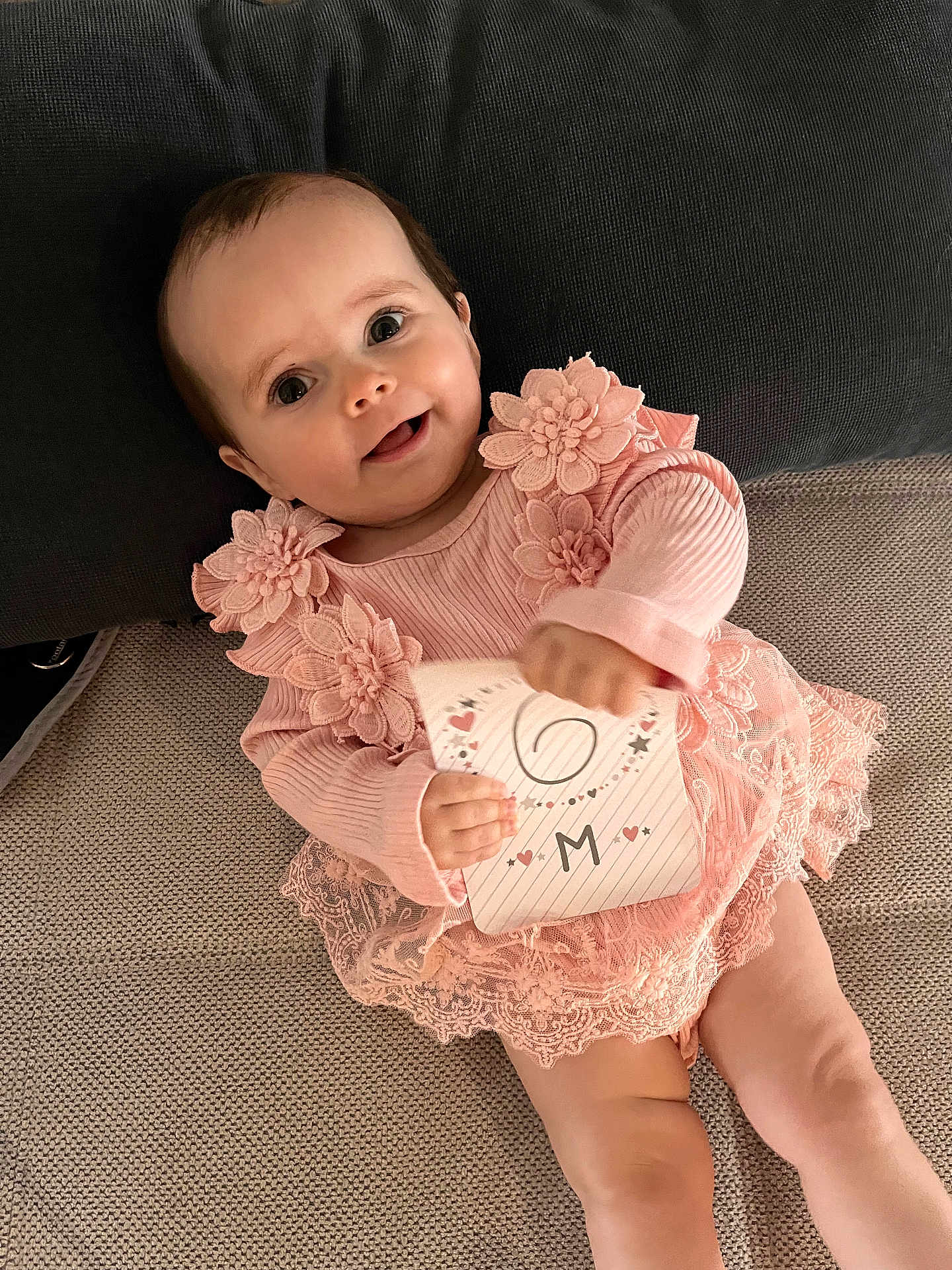 Thalya participe au concours pour gagner de l'argent avec cette photo : baby, card, child, closeup, couch, cute, fabric, happy, holding_object, indoor, infant, lace, person, pillow, pink_dress, portrait, sitting, six_months, smiling, young_child