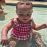 baby, child, infant, swimming_pool, water, outdoor, summer, sunlight, pink_outfit, swimsuit, wet_hair, sitting, portrait, face, poolside, trees, lounge_chairs, reflection, shallow_water, happy