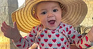 Gianna is registered to the contest to win money with this photo: baby, child, infant, sunhat, strawberry, patterned_clothing, smiling, happy, open_mouth, outdoor, patio, sunlight, portrait, seated, table, stone_wall, wooden_roof, summer, fashion, playful