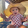 baby, child, infant, sunhat, strawberry, patterned_clothing, smiling, happy, open_mouth, outdoor, patio, sunlight, portrait, seated, table, stone_wall, wooden_roof, summer, fashion, playful