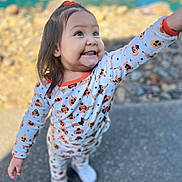 Sariyah is registered to the contest to win money with this photo: child, toddler, girl, smiling, happy, outdoor, portrait, standing, reaching, pajamas, pumpkin_pattern, long_hair, hair_bow, socks, playful, daylight, pavement, blurred_background, close_up, full_body