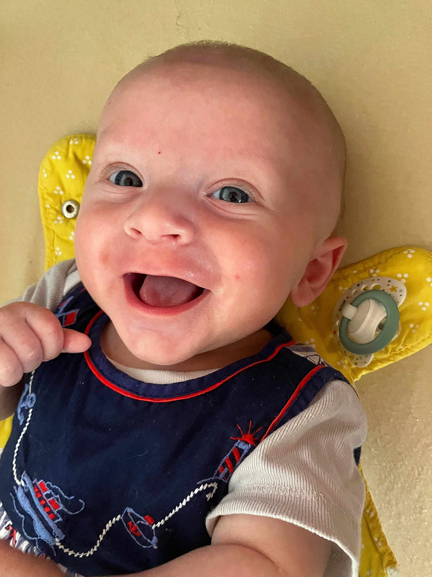 Lucas a rejoint le concours — aidez-le/la à gagner de superbes lots ! baby, smiling, happy, infant, face, blue_eyes, clothing, navy_blue, pacifier, yellow_cushion, lying_down, cute, child, skin, expression, mouth_open, hand, short_sleeves, indoors, portrait