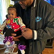 Elyvia joined the competition — help win amazing prizes! baby, adult, indoor, holding, colorful_clothing, purple_bows, shoes, hat, jacket, television, smiling_faces, curtains, floor, wooden_floor, person, family, child, portrait, casual, home