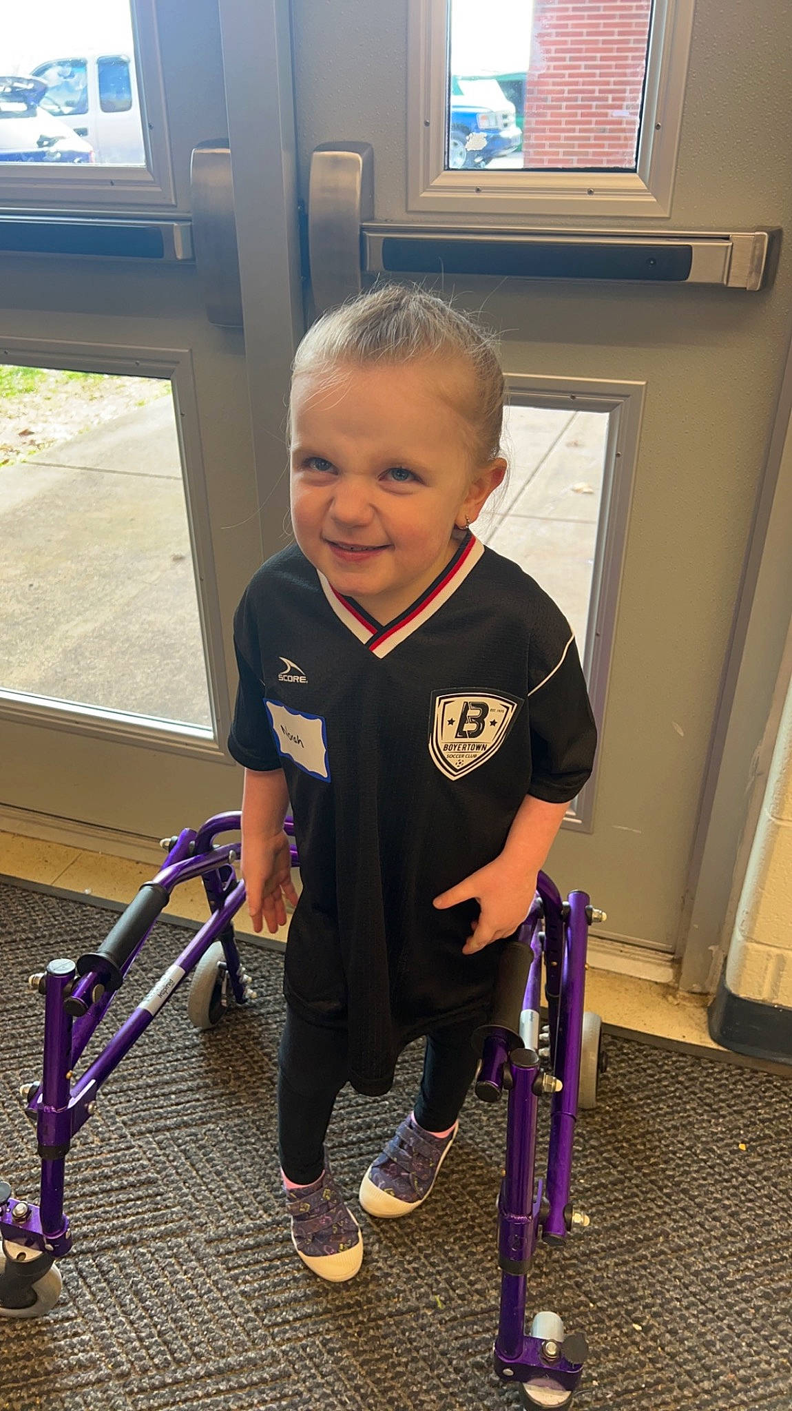 Norah is registered to the contest to win money with this photo: baby, baby_carriage, baby_products, baby_toddler_clothing, bicycle_frame, bicycle_tire, child, electric_blue, flooring, fun, joy, leg, person, picture_frame, play, smile, sneakers, standing, t_shirt, television