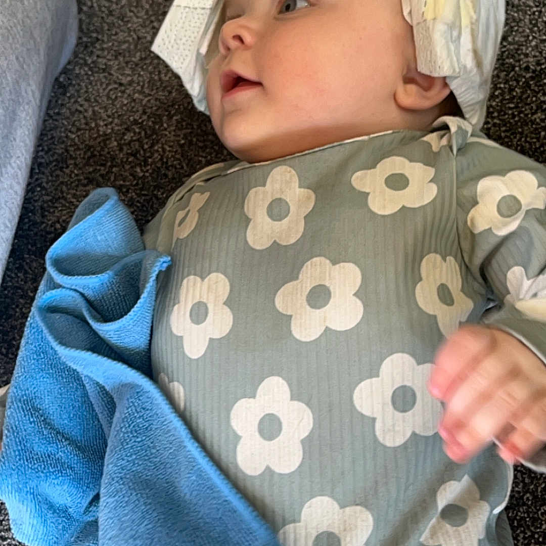 Athena is registered to the contest to win money with this photo: baby, blanket, bodypart, bonnet, cap, clothing, dress, face, finger, hand, hat, head, hood, longsleeve, newborn, person, photography, portrait, sleeve, t_shirt