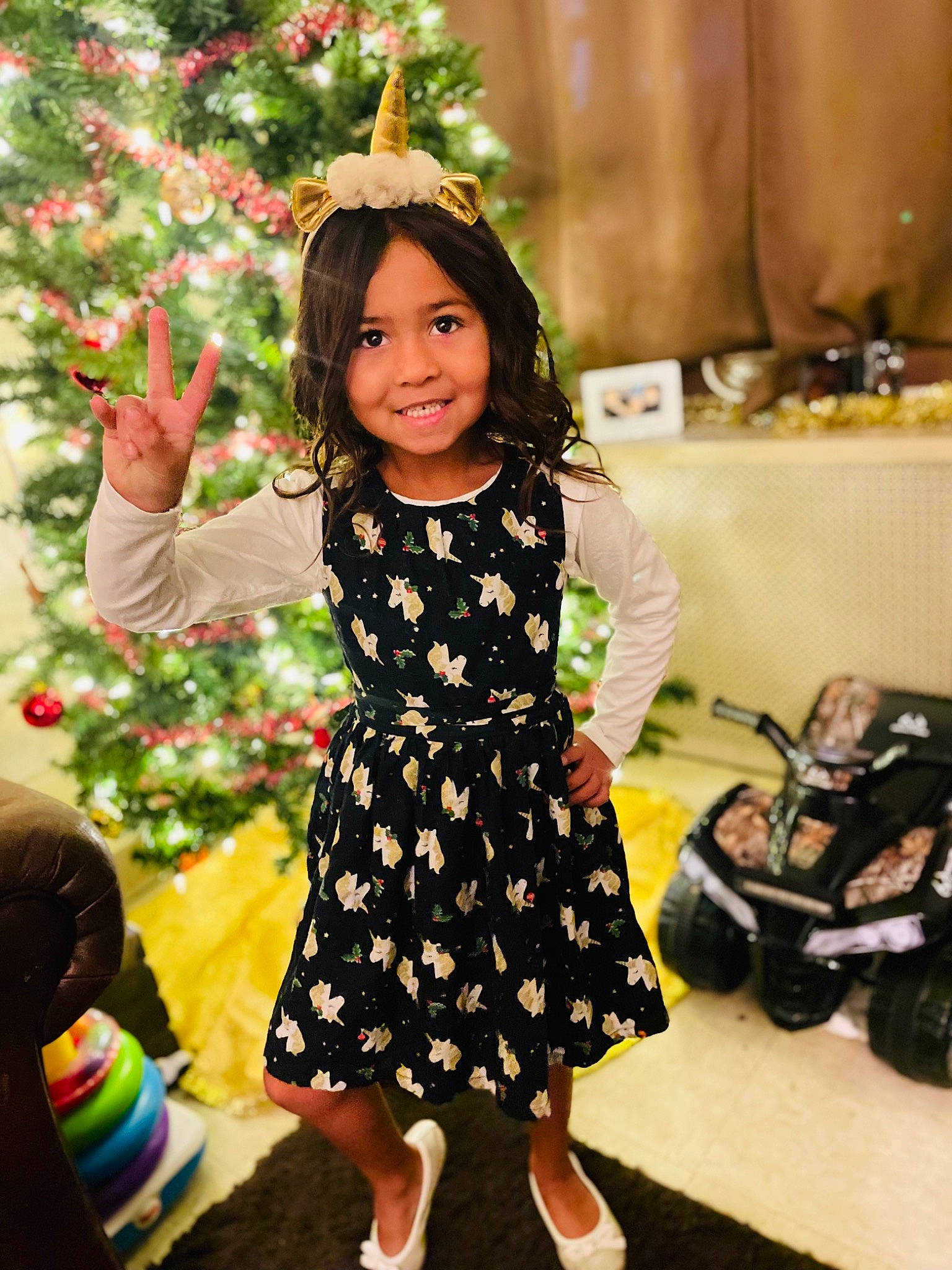 Adelina is registered to the contest to win money with this photo: christmas_decoration, christmas_ornament, christmas_tree, dress, facial_expression, fun, hairstyle, happy, head, joy, one_piece_garment, ornament, people_in_nature, person, skin, sleeve, smile, standing, toddler, tree