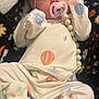 baby, infant, pacifier, pacifier_clip, headband, bow, onesie, hot_air_balloon, blanket, pattern, booties, mittens, beads, portrait, close_up, cozy, soft_fabric, newborn_style, indoors, sleepwear