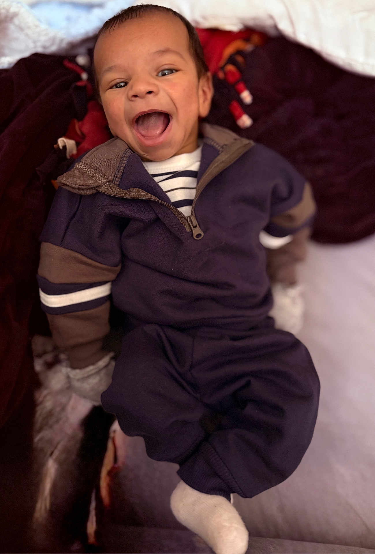 Kashmier joined the competition — help win amazing prizes! baby, infant, smiling, laughing, open_mouth, face, head, clothing, zip_jacket, striped_shirt, mittens, sock, blanket, bed, cozy, portrait, indoor, happy, adorable, sitting