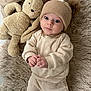 baby, infant, hat, knitwear, beige, stuffed_animal, bunny, plush_toy, rug, soft_texture, cute, child, indoor, clothing, portrait, lying_down, hands, expression, cozy, adorable