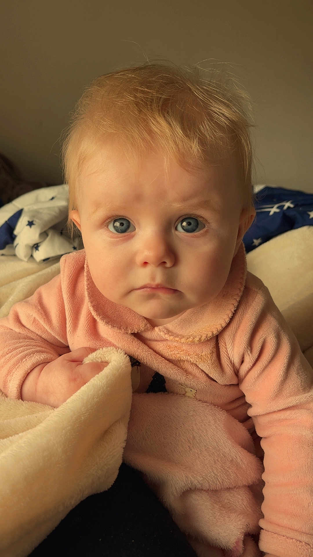 Alice a rejoint le concours — aidez-le/la à gagner de superbes lots ! baby, child, infant, face, blue_eyes, blonde_hair, blanket, clothing, pink_outfit, hand, portrait, indoor, soft_light, expression, young_child, cute, fuzzy_texture, cozy, warm_tones, looking_at_camera