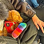 puppy, dog, sleeping, red_harness, plush_toy, rainbow, hand, jeans, car_interior, seat, clothing, casual, fur, resting, cute, cozy, pet, lap, relaxed, colorful