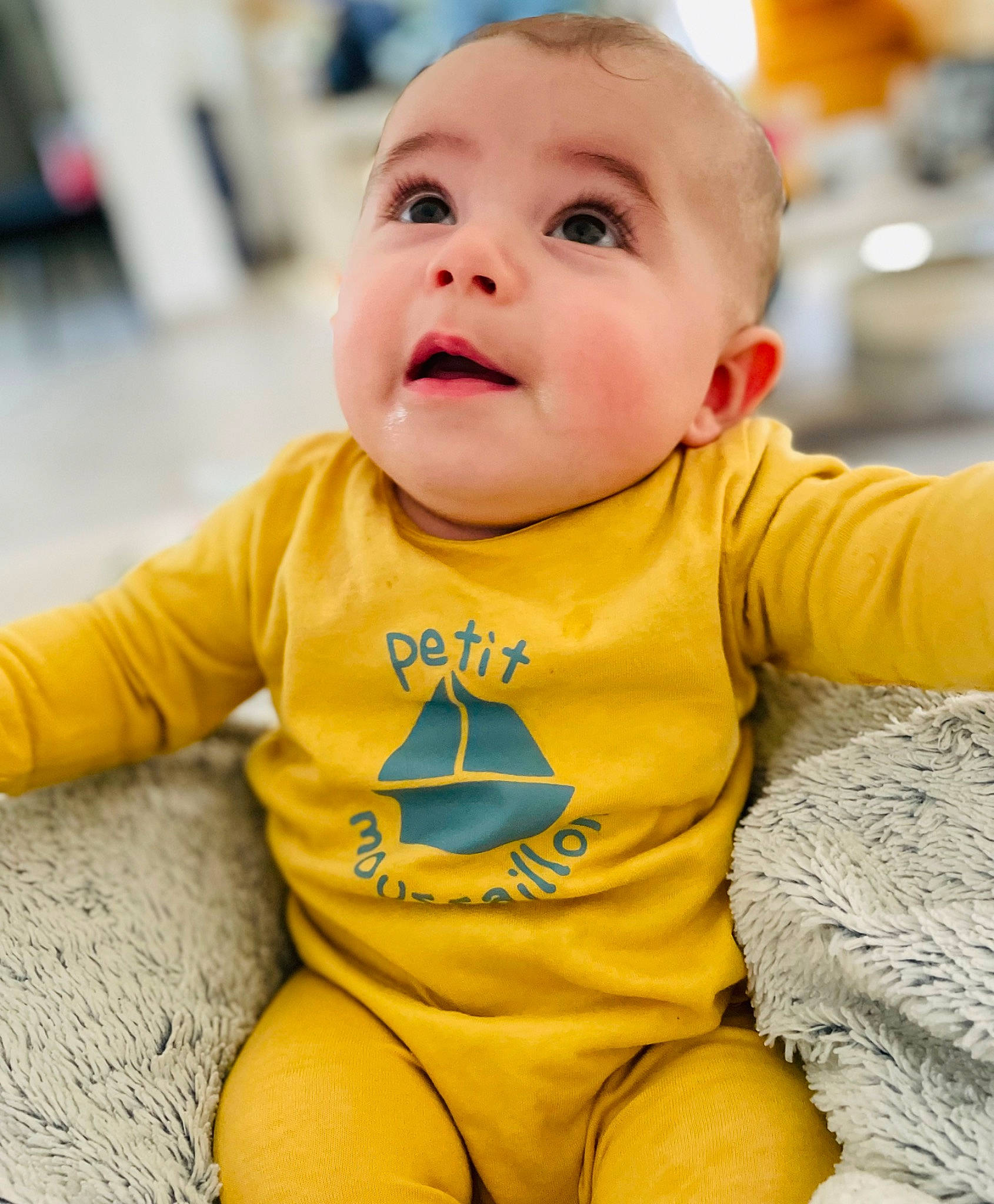Mylio participe au concours pour gagner de l'argent avec cette photo : baby, baby_toddler_clothing, cheek, child, eye, face, flooring, fun, happy, head, iris, long_sleeved_t_shirt, outerwear, person, product, sitting, skin, sleeve, smile, t_shirt