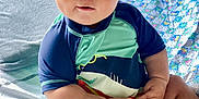 John is registered to the contest to win money with this photo: baby, child, indoor, bed, toy, clothing, blue, green, person, cute, face, hair, hands, legs, sitting, bedroom, lamp, quilt, looking, play