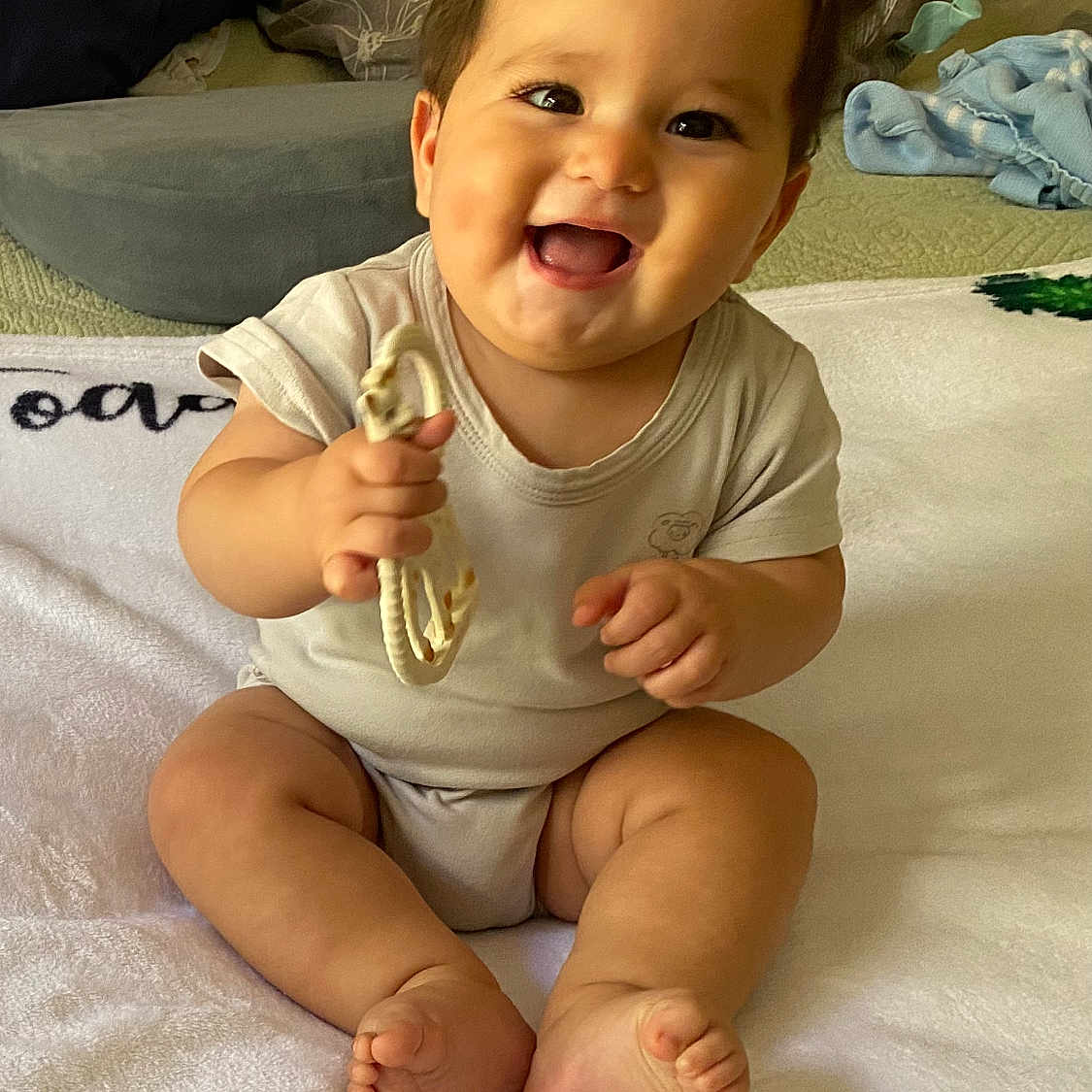 John is registered to the contest to win money with this photo: baby, blanket, child, clothing, cushion, cute, face, foot, hand, happy, home, indoors, infant, person, portrait, sitting, skin, smiling, soft, teething_toy