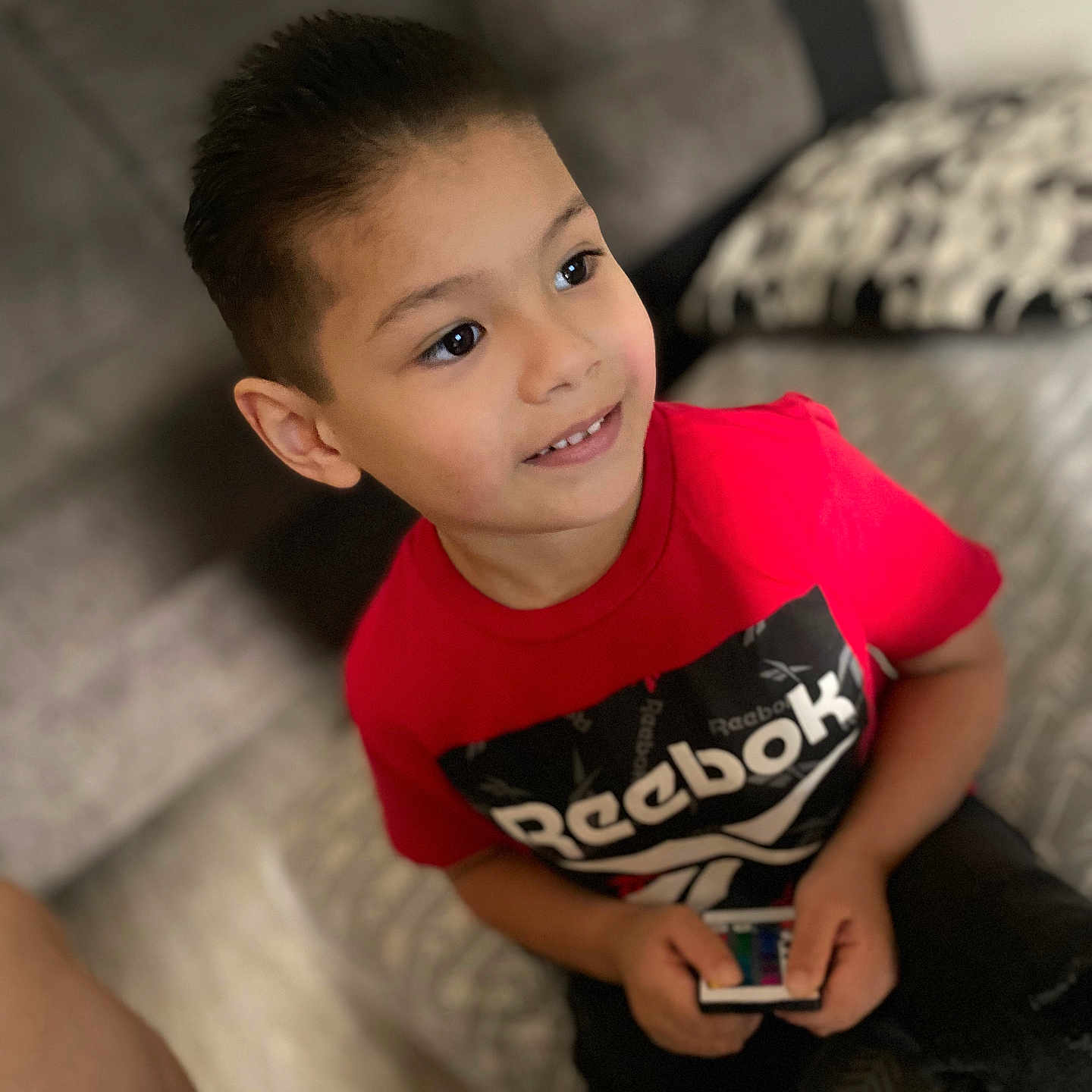 Mateo is registered to the contest to win money with this photo: bodypart, boy, child, clothing, couch, electronics, face, finger, furniture, hand, head, male, mobilephone, pants, person, phone, photography, portrait, sitting, t_shirt