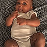 baby, infant, onesie, lying_down, blanket, patterned_blanket, curious_expression, chubby_cheeks, barefoot, indoor, cute, child, skin, face, head, limbs, newborn, person, soft_texture, cozy