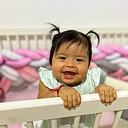 Yumi participe au concours pour gagner de l'argent avec cette photo : baby, child, smiling, crib, pigtails, infant, happy, indoor, toy, braided_bumper, white, cute, face, person, hand, clothing, playful, room, portrait, toddler