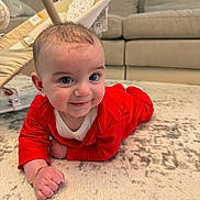 Giovanni joined the competition — help win amazing prizes! baby, infant, red_clothing, bracelet, carpet, floor, smile, face, indoor, couch, furniture, baby_gear, happy, child, person, home, cute, lying_down, young, bright