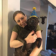 Davinci Charles is registered to the contest to win money with this photo: animal, black_dog, casual_clothing, celebration, dog, friendship, furniture, happy, headwear, home_interior, hugging, indoor, lamp, living_room, party_hat, person, pet, smiling, wall, woman