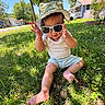 Luka is registered to the contest to win money with this photo: baby, child, grass, sunglasses, hat, outdoor, summer, sunny, greenery, barefoot, casual_clothing, house, trees, daylight, nature, cute, portrait, sitting, toddler, playful