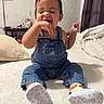 baby, child, toddler, denim_overalls, shoes, smiling, happy, indoors, bed, blanket, pillow, person, cute, sitting, expression, face, clothing, footwear, home, cozy