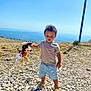 Lemony participe au concours pour gagner de l'argent avec cette photo : blue_sky, child, curly_hair, grass, hill, mickey_mouse, nature, outdoor, person, plush_toy, pole, rocky_ground, sandals, shadow, shorts, standing, sunny, toddler, toy, tshirt