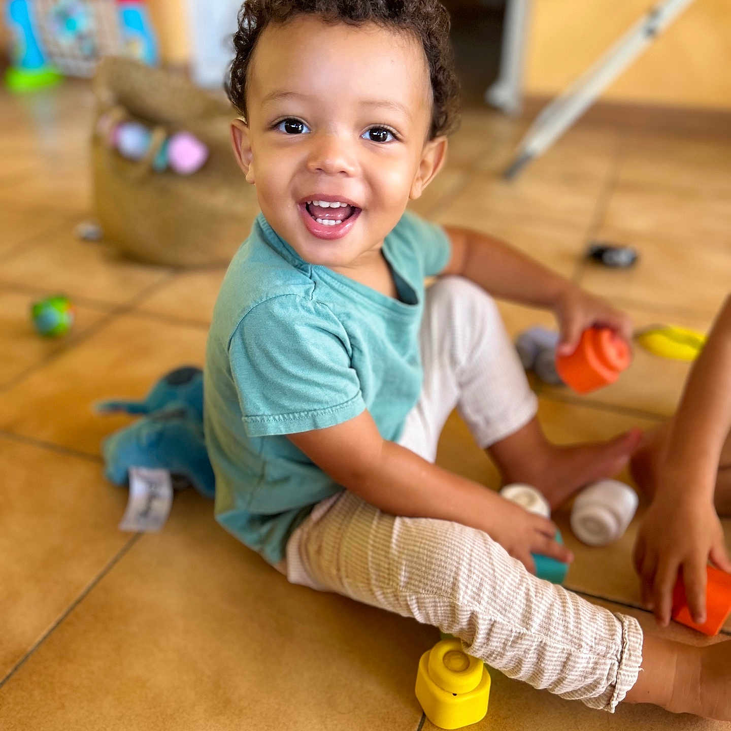 Lemony a rejoint le concours — aidez-le/la à gagner de superbes lots ! barefoot, bright, casual_clothing, child, colorful, curly_hair, cute, floor_tiles, fun, happy, home, indoor, person, playing, playtime, smiling, stacking_cups, toddler, toys, young_child