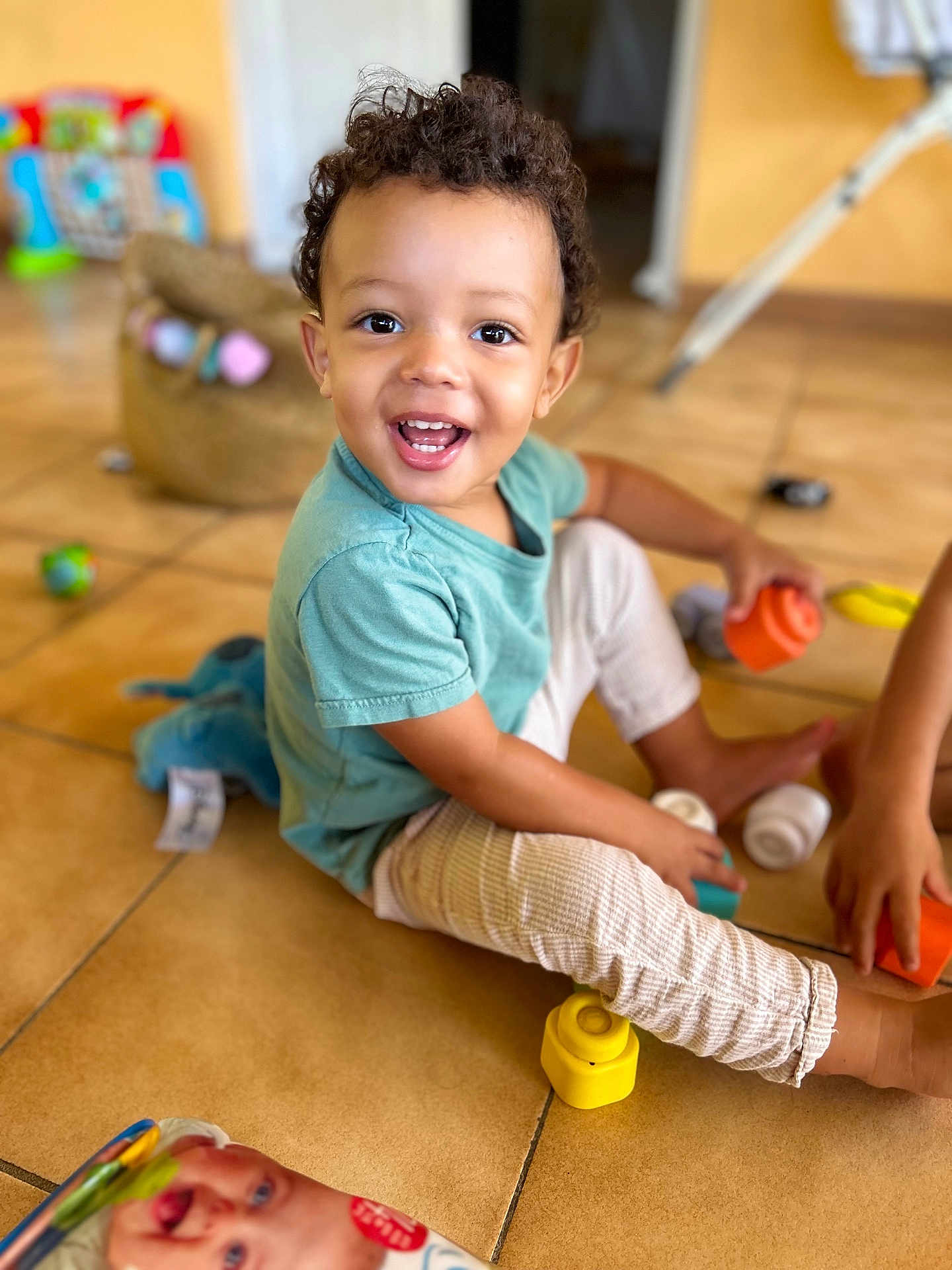 Lemony a rejoint le concours — aidez-le/la à gagner de superbes lots ! barefoot, bright, casual_clothing, child, colorful, curly_hair, cute, floor_tiles, fun, happy, home, indoor, person, playing, playtime, smiling, stacking_cups, toddler, toys, young_child