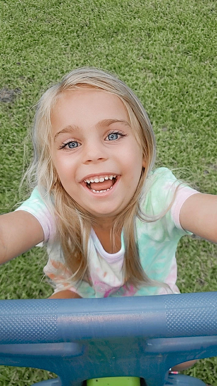 Abbigale Lynn is registered to the contest to win money with this photo: blond, child, child_model, face, facial_expression, fun, grass, hair, happy, head, joy, laugh, leisure, mouth, person, play, playground, public_space, sitting, smile