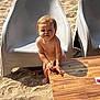 toddler, child, diaper, sand, beach, table, wood, chair, plastic_chair, sunlight, outdoor, shadow, curious, standing, baby, person, skin, face, hands, foot