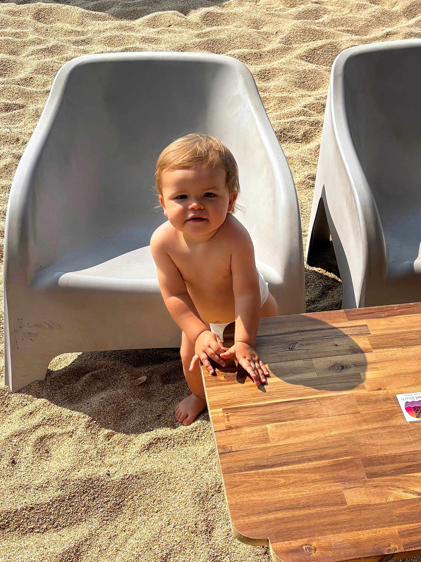 Alessio participe au concours pour gagner de l'argent avec cette photo : toddler, child, diaper, sand, beach, table, wood, chair, plastic_chair, sunlight, outdoor, shadow, curious, standing, baby, person, skin, face, hands, foot