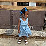 Leilani is registered to the contest to win money with this photo: child, girl, blue_bows, braided_hair, dress, sandals, concrete, steps, wooden_railings, outdoor, side_view, patterned_dress, young_child, standing, solemn_expression, urban_environment, daylight, summer_clothing, person, casual