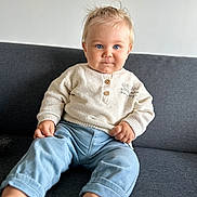 Milan a rejoint le concours — aidez-le/la à gagner de superbes lots ! baby, child, sitting, indoor, couch, blue_eyes, sweater, pants, barefoot, blond_hair, portrait, cute, infant, casual_clothing, home, smiling, person, furniture, relaxed, light