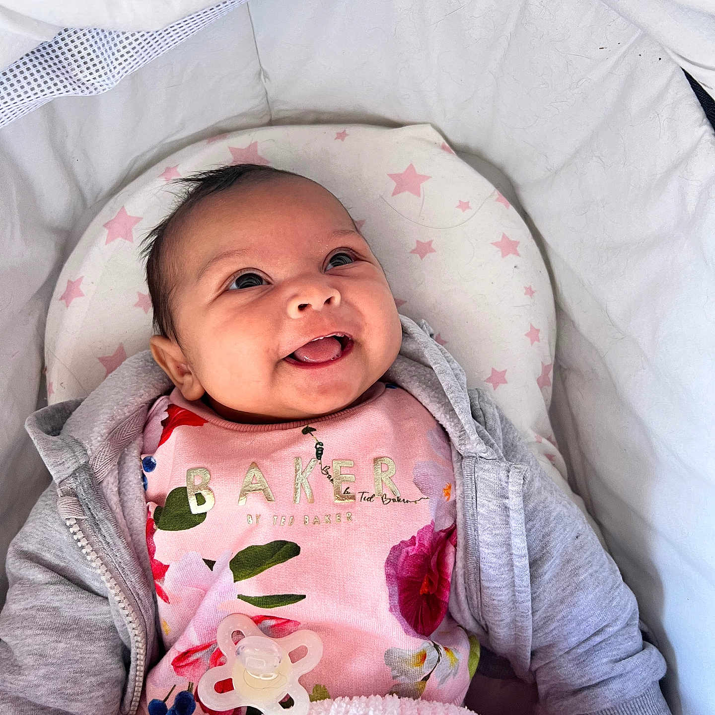 Mabel joined the competition — help win amazing prizes! baby, blanket, clothing, cozy, cushion, cute, face, happy, hoodie, indoors, infant, lying_down, pacifier, person, pink, portrait, smiling, soft_texture, star_pattern, young_child