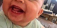 Mabel joined the competition — help win amazing prizes! baby, smiling, laughing, close_up, infant, green_clothing, indoor, living_room, table, lamp, person, happy, cute, face, young_child, human, sitting, joyful, child, apparel