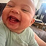 baby, smiling, laughing, close_up, infant, green_clothing, indoor, living_room, table, lamp, person, happy, cute, face, young_child, human, sitting, joyful, child, apparel