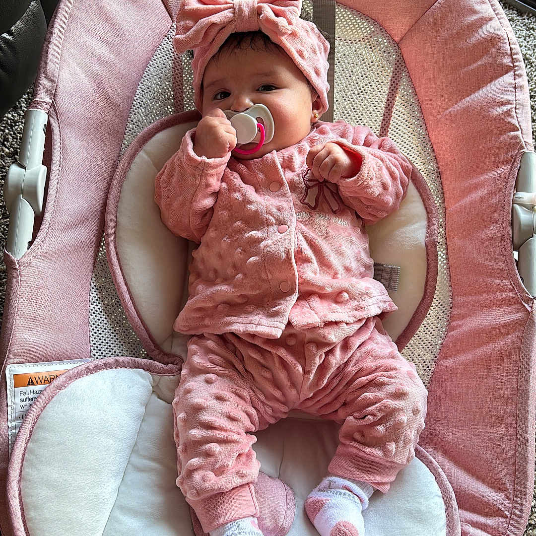 Lorena is registered to the contest to win money with this photo: baby, infant, pacifier, pink_clothing, headband, baby_seat, carpet, indoors, cute, child, plush, soft_texture, relaxing, portrait, small_person, sock, cozy, baby_girl, comfort, wearing