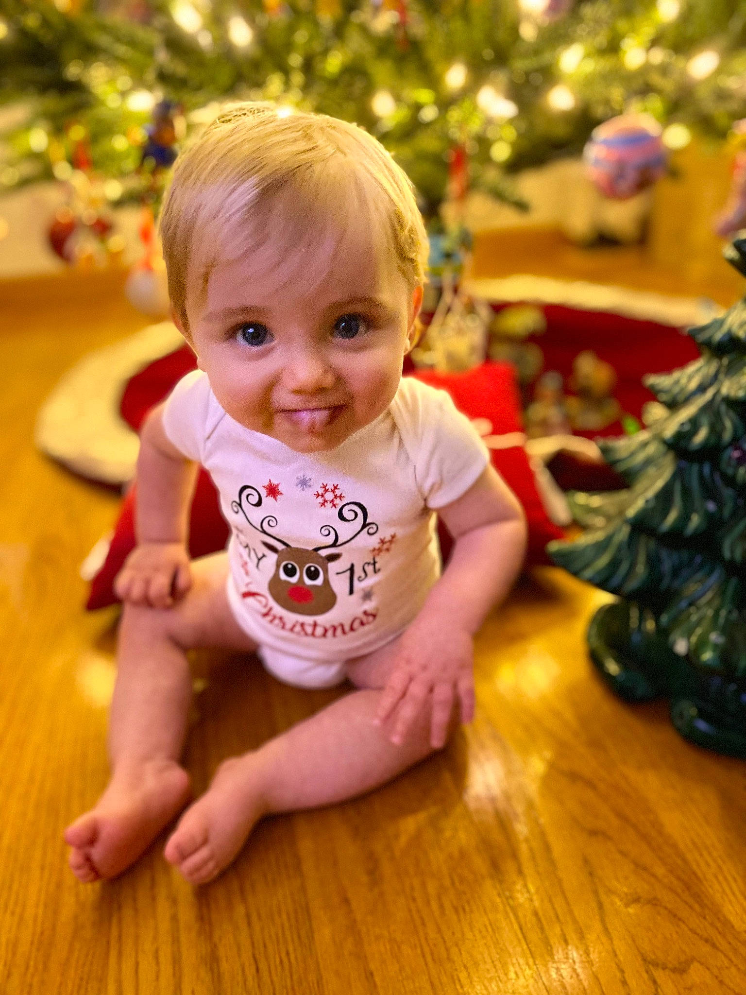 Carmine is registered to the contest to win money with this photo: baby, baby_toddler_clothing, cheek, child, christmas_ornament, christmas_tree, event, eye, facial_expression, flooring, fun, happy, hardwood, holiday, ornament, person, sitting, skin, smile, toddler