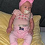 Hadley is registered to the contest to win money with this photo: baby, infant, pink_clothing, headband, pacifier, blanket, socks, sitting, indoors, baby_bottle, snacks, shelf, wall, face, person, cute, young_child, comfort, rest, soft_texture