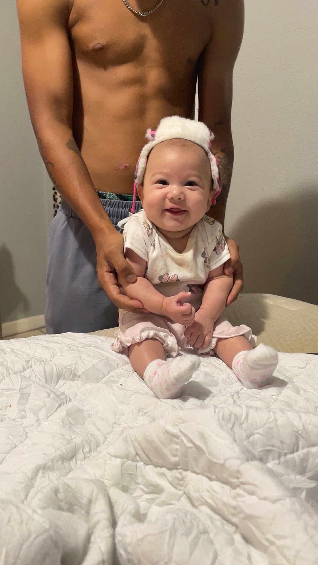 Hadley is registered to the contest to win money with this photo: baby, infant, smiling, hat, socks, shirtless_adult, tattoos, hands, bed, quilt, white, indoor, person, family, supporting, cute, happy, child, clothing, skin